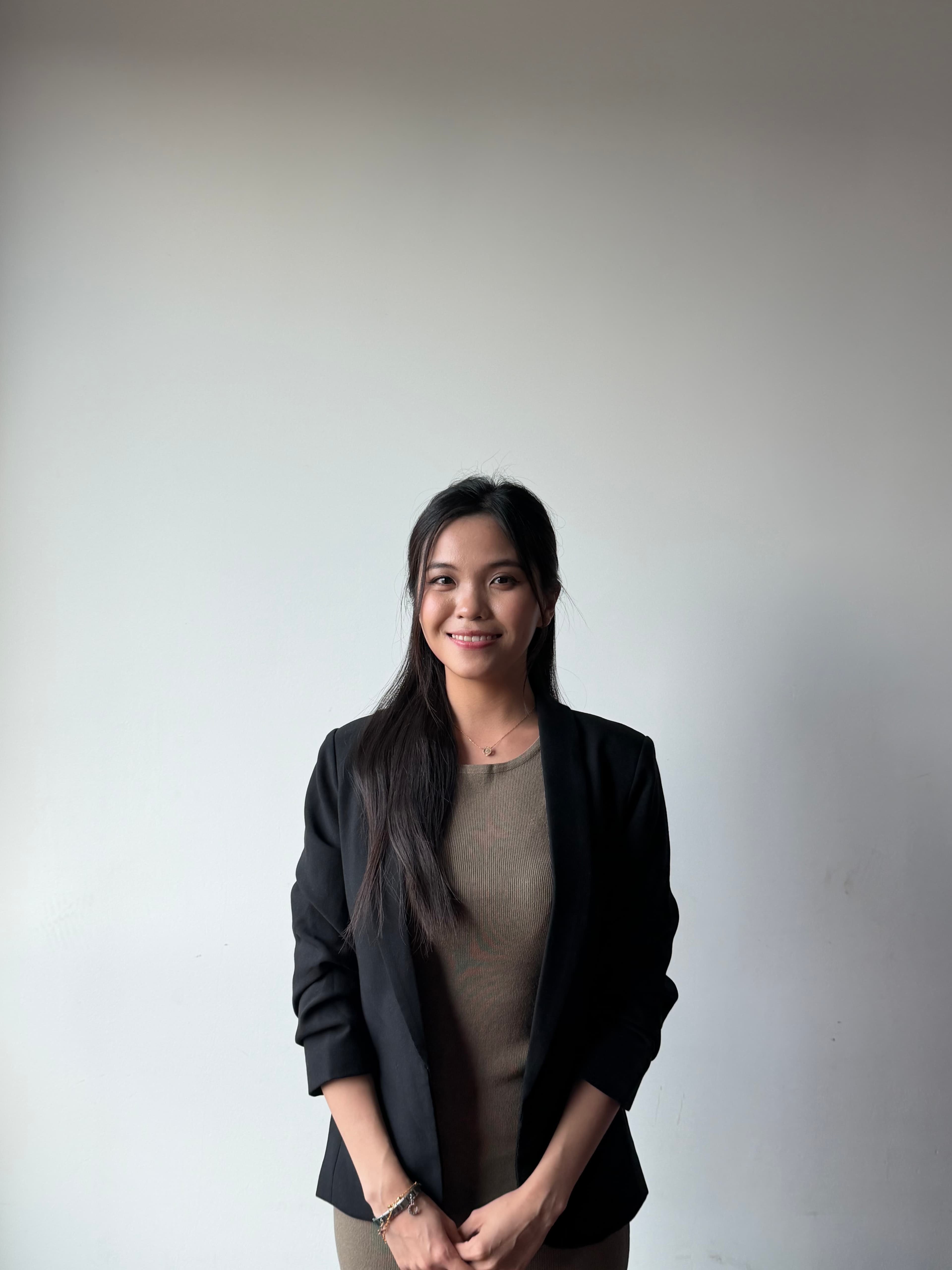 Smiling woman with long dark hair wearing a black blazer over a brown top.